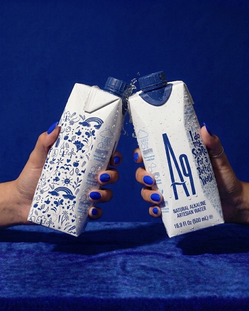 Two people raising cold A9 natural alkaline water cartons against a deep blue background